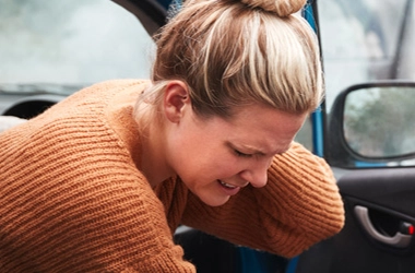 Woman sitting in her car, holding her neck with a pained expression.