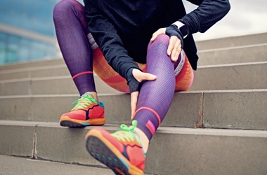 Person sitting on stairs wearing sportswear, holding their knee.